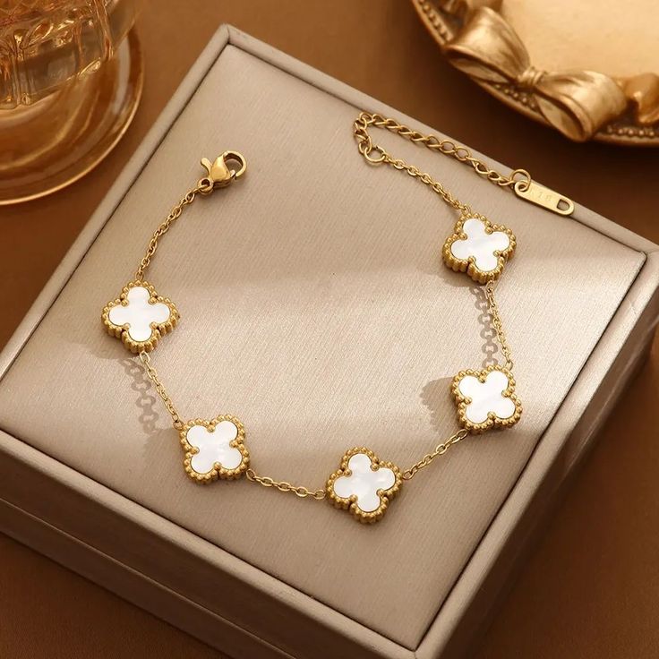Pulsera de trébol dorada con dijes blancos dentro de una caja de presentación